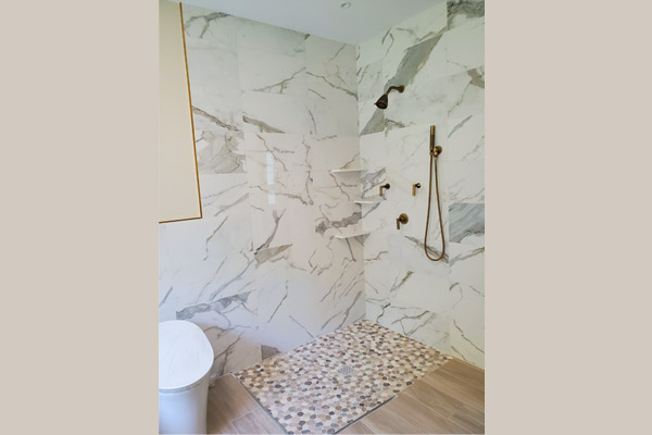 Walk-in shower with pebble flooring and brass fixtures beside the Oasis Hammock Bath in a New Jersey home.